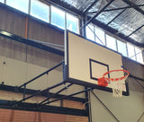 Wall-mounted fiberglass basketball backboard with black target, border, and orange rim in a gym.
