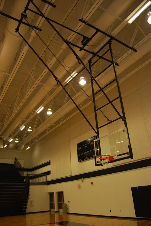 Ceiling-hung basketball backstop with a glass backboard and red hoop in a gymnasium.