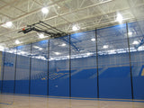 Blue roll-up gymnasium curtain separating a basketball court from bleachers.