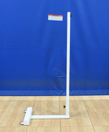 White portable badminton net post with a wheeled base, set against a blue wall and wood floor.