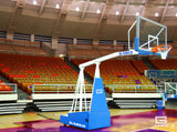 Portable basketball hoop with clear backboard and orange rim on a court in an empty arena.