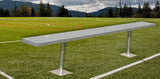 Long gray bench with two posts on a green turf field with white lines.