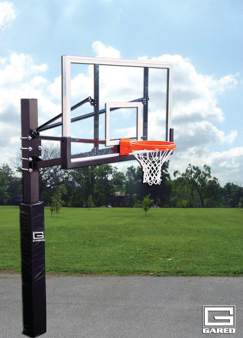 Basketball hoop with clear backboard, orange rim, and white net on a black pole with padding, outdoors.