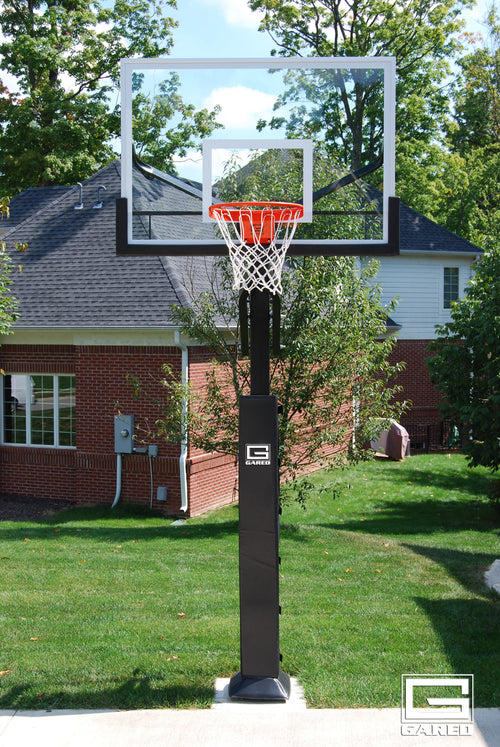 Adjustable basketball hoop with a clear glass backboard and orange rim in a backyard.