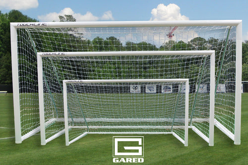Three white soccer goals of varying sizes, nested together on a green field under a blue sky.