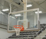 Glass basketball backboard with orange rim and white net in a gym with empty bleachers.