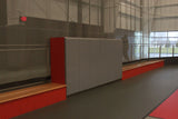 Gray wall pads with red end caps installed above red benches in a large indoor facility.