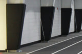 Black column wall pads installed on a white brick wall next to a running track.