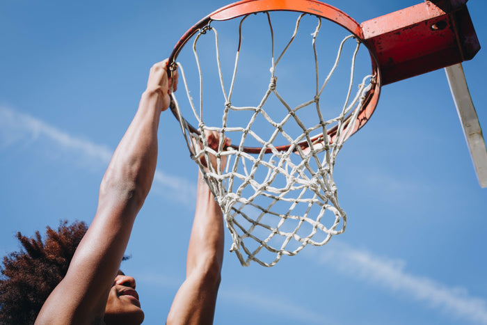 Basketball player hanging from the rim after a dunk during a game