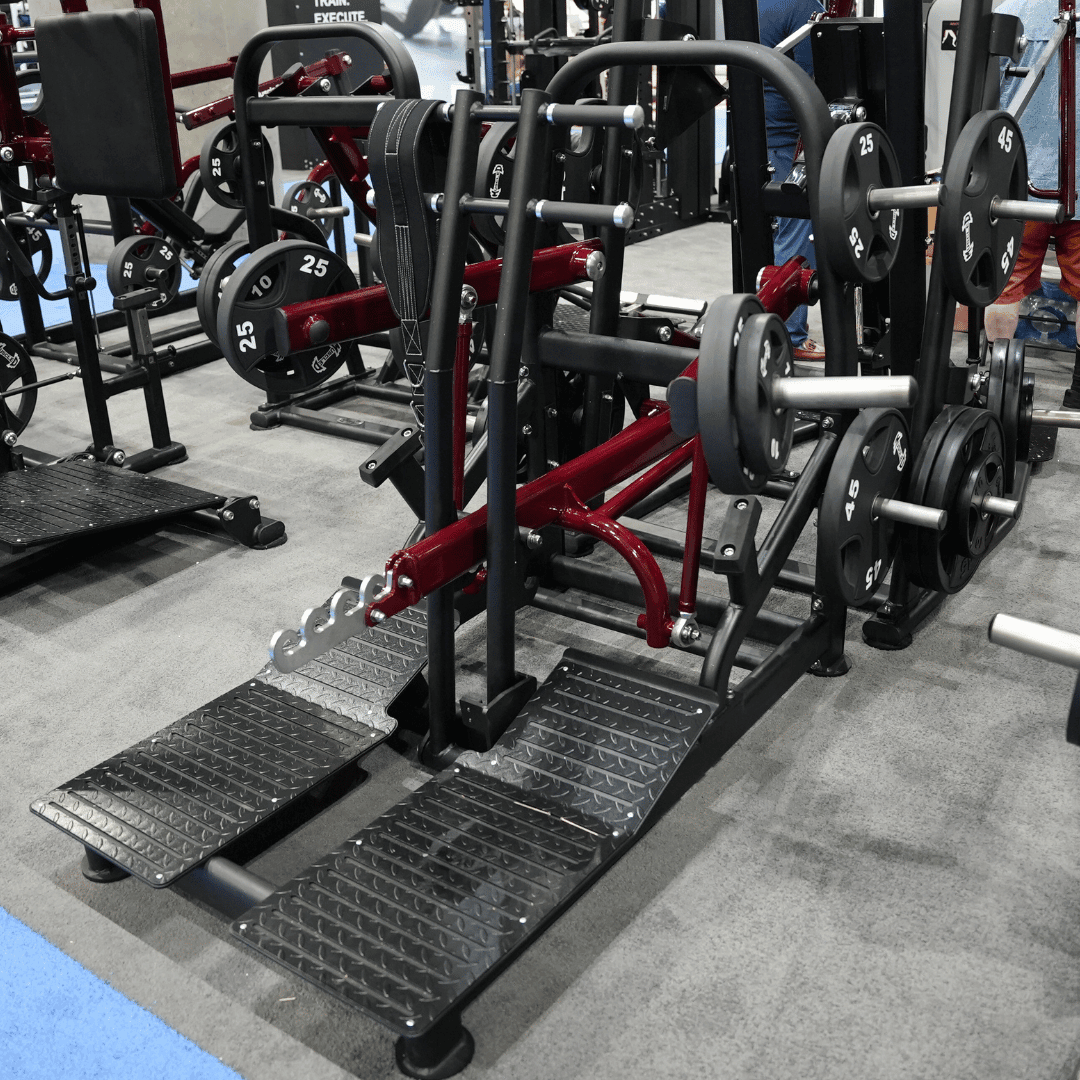 Black and red plate-loaded belt squat machine with textured foot platforms.