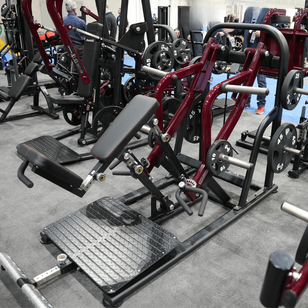 Red and black chest-supported plate-loaded row machine with a padded seat and footrests in a gym setting.