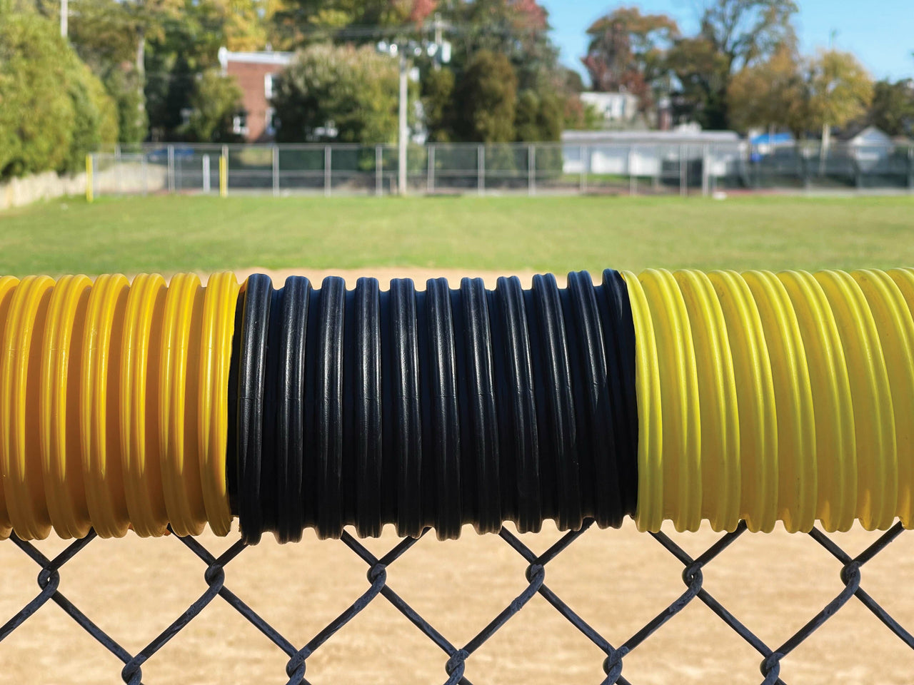 Three colors of chain link fence topper being demonstrated on a baseball field