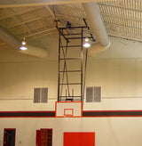 Ceiling-mounted basketball backstop with a white backboard and orange rim in a gymnasium.
