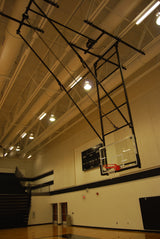 Ceiling-hung basketball backstop with a glass backboard and red hoop in a gymnasium.