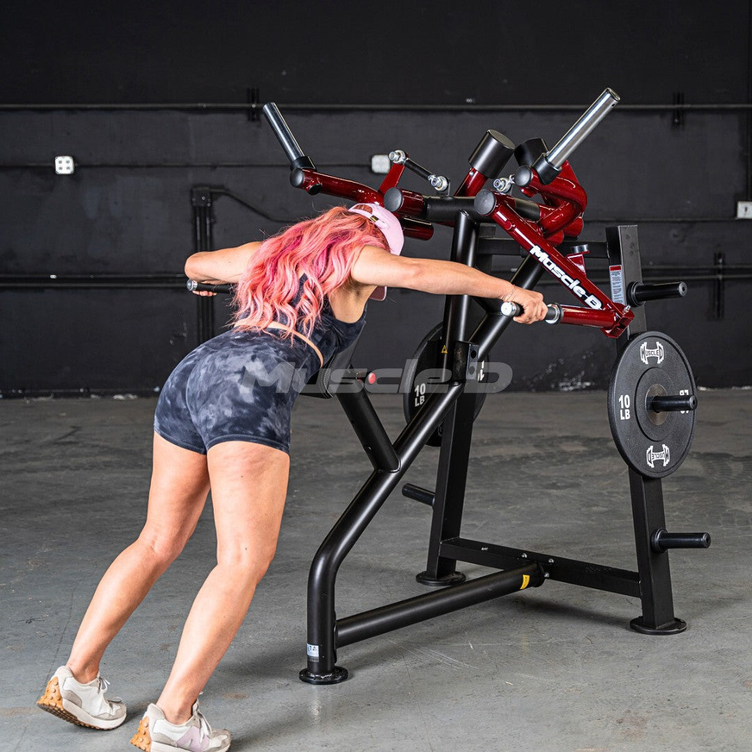 Woman with pink hair using a red and black rear delt machine in a gym.