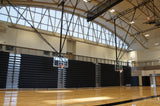 Ceiling-hung basketball backstop with a clear backboard and orange rim in a gym with bleachers.