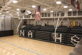 Two ceiling-hung basketball backstops with bent single posts in a gymnasium with bleachers.