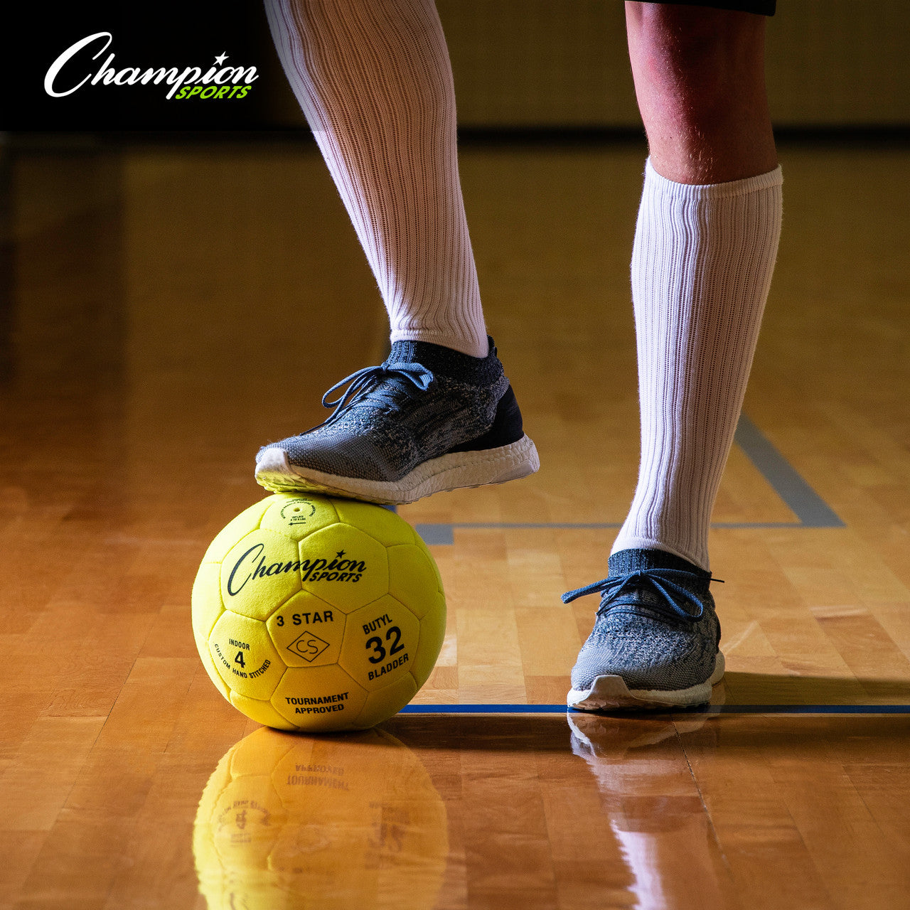 Player's foot on a yellow Champion Sports 3-Star indoor soccer ball on a gym court.