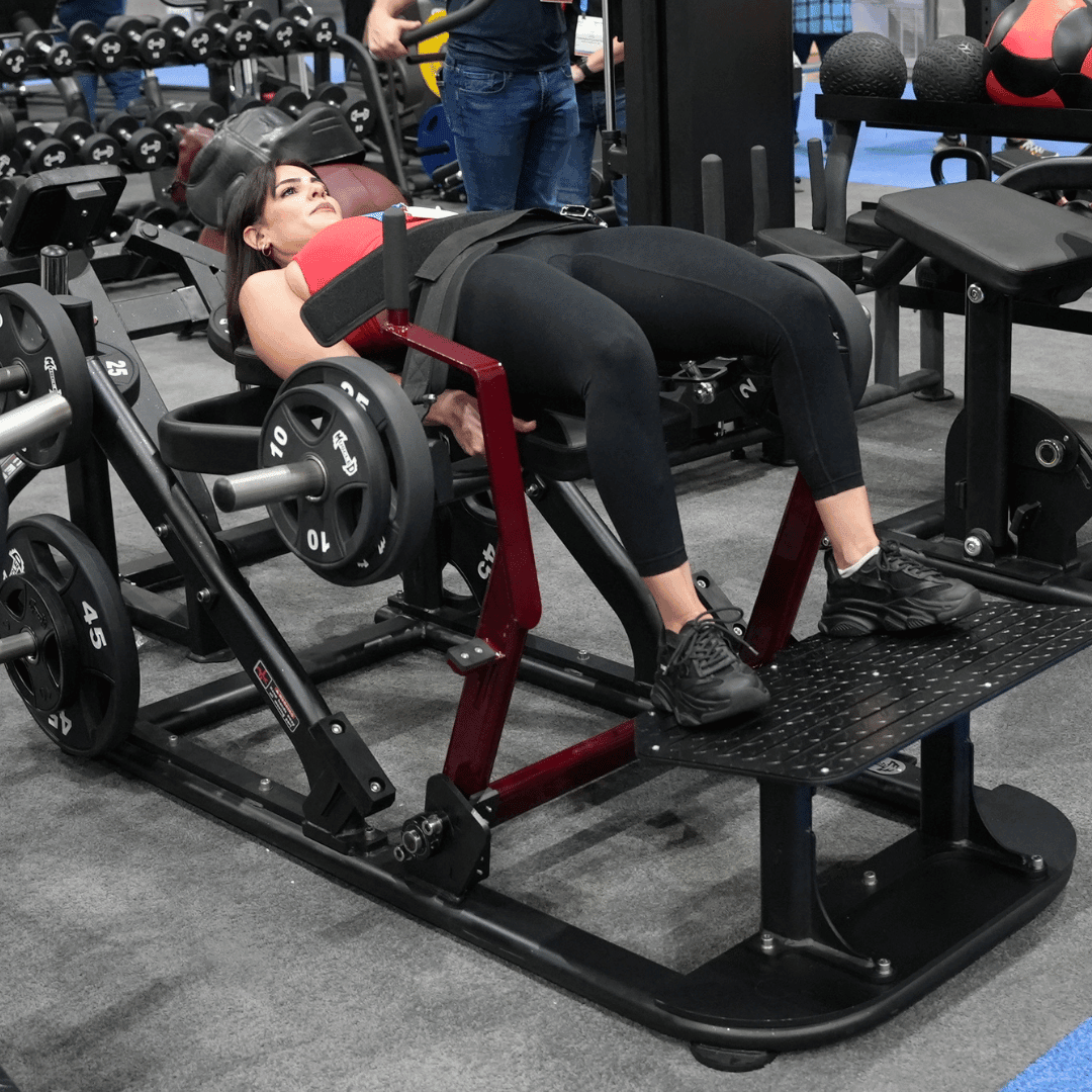 Woman using a plate-loaded hip thruster machine in a gym.