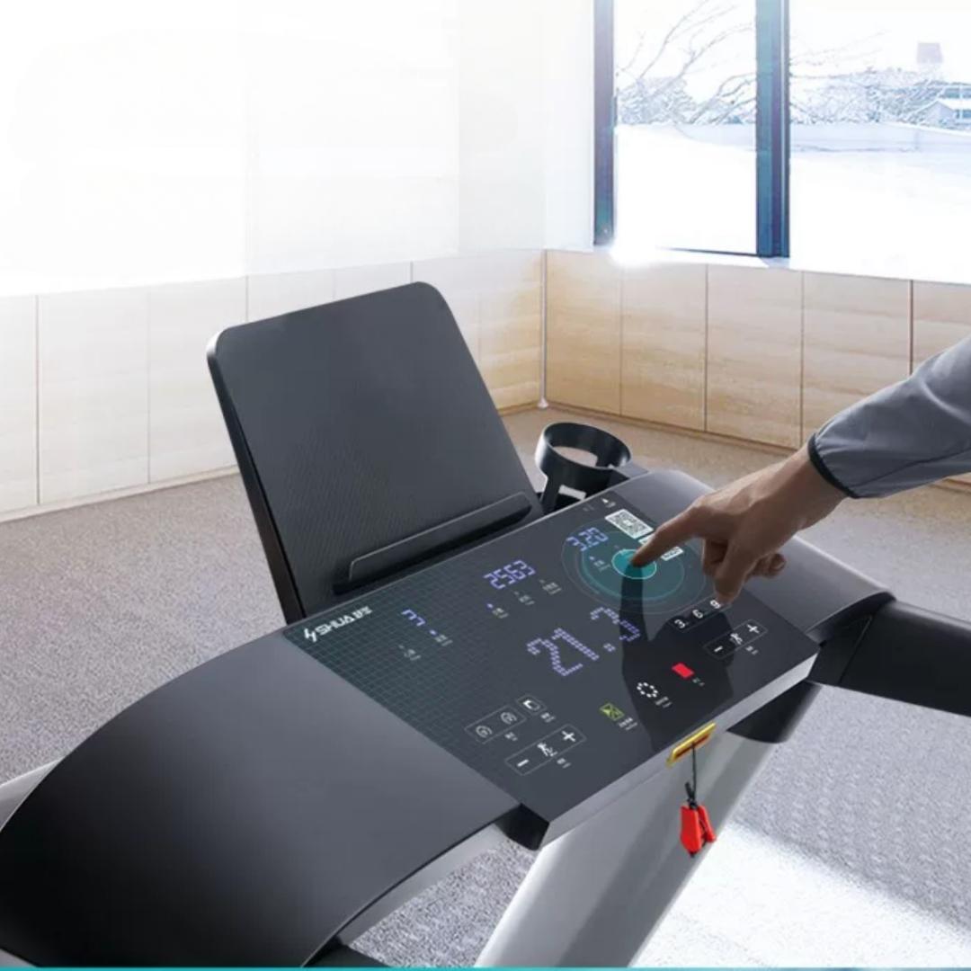 Hand touching the LED console of a black treadmill with a cup holder and tablet stand.