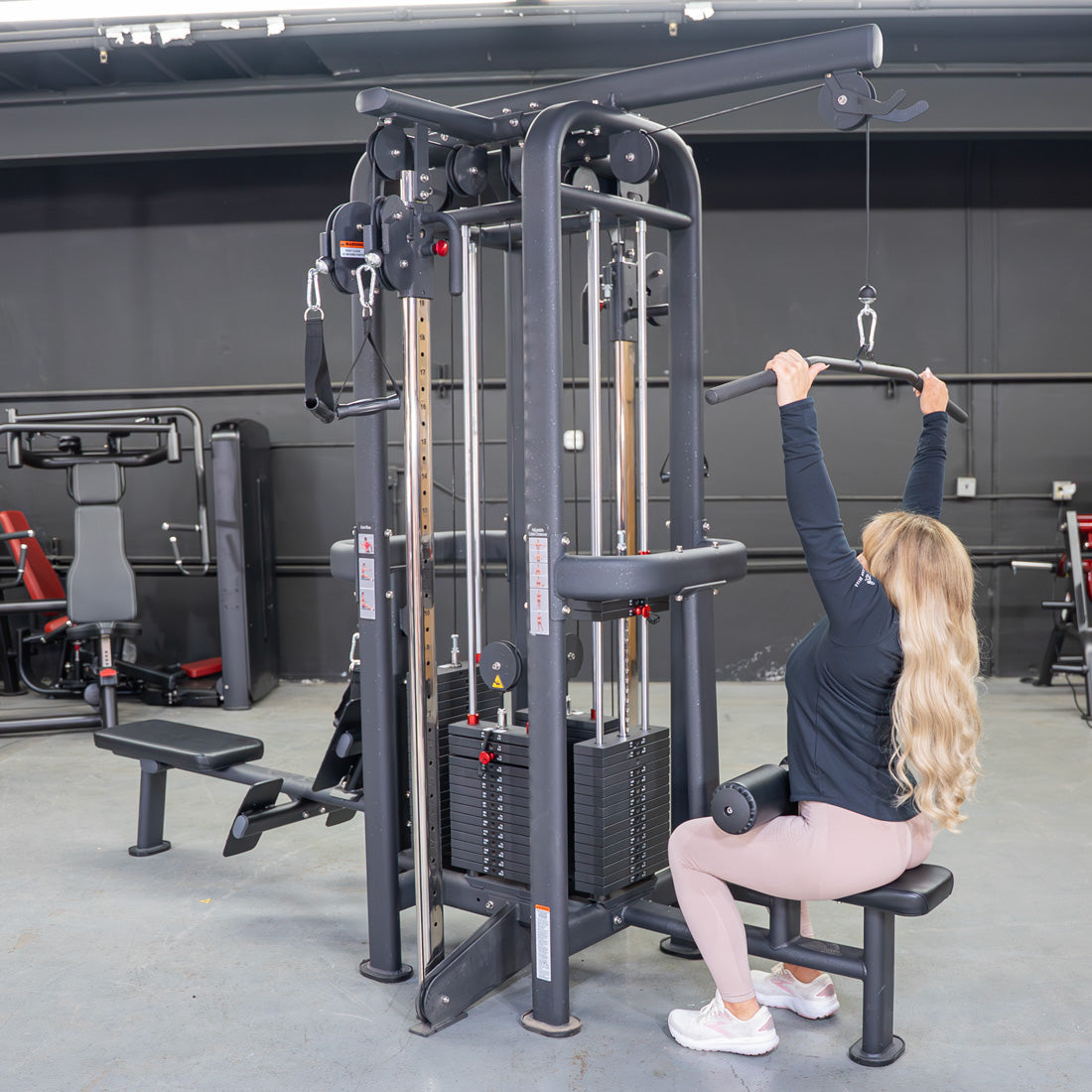 Woman doing lat pulldowns on a black 4-stack jungle gym in a gym.
