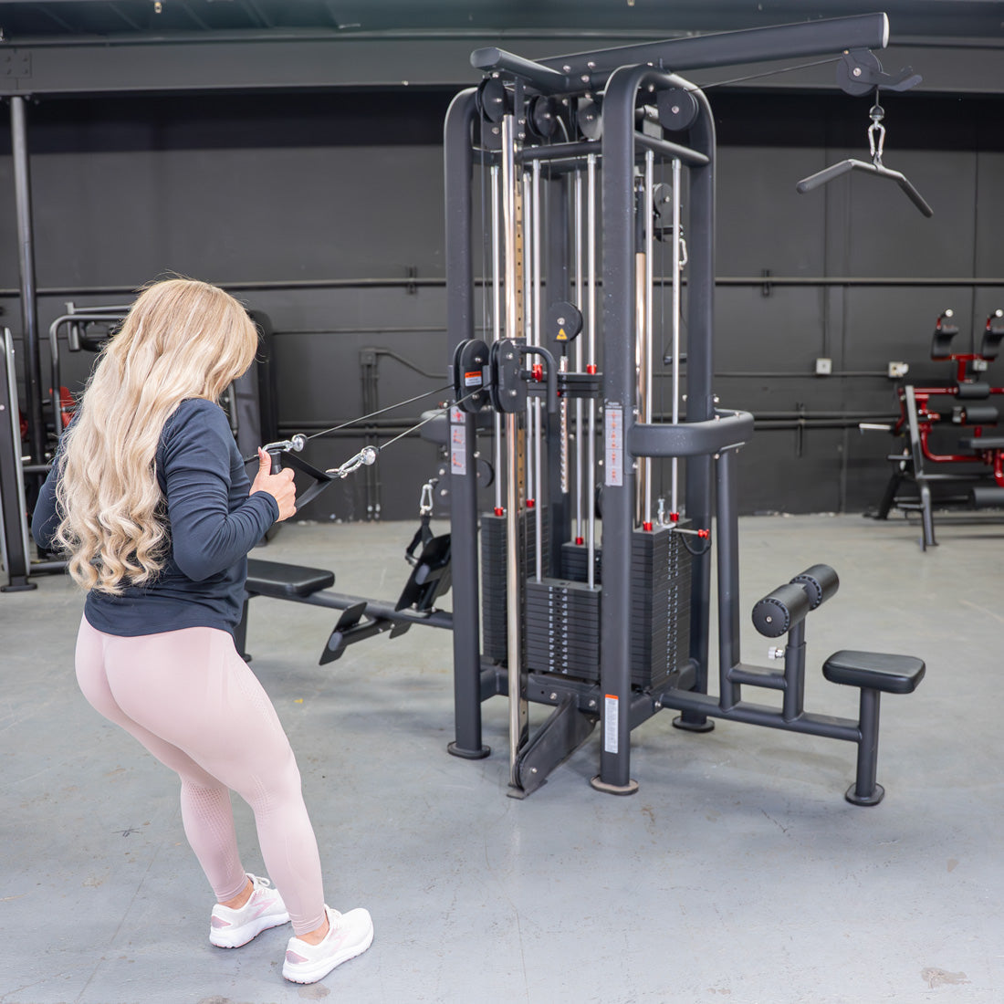 Woman using a 4-stack jungle gym with multiple cable pulleys and weight stacks in a gym.