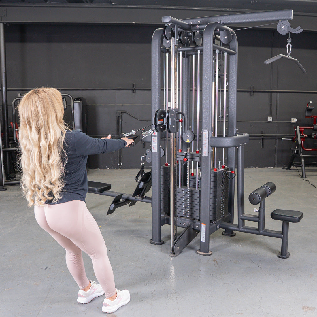 Woman doing a low row on a 4-stack jungle gym machine with multiple pulleys and weight stacks in a gym.