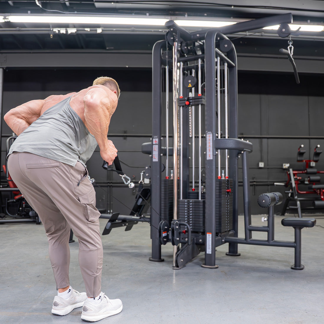 Man in a tank top using a black 4-stack jungle gym cable machine for a low row exercise in a gym.