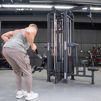 Thumbnail for Man in a tank top using a black 4-stack jungle gym cable machine for a low row exercise in a gym.