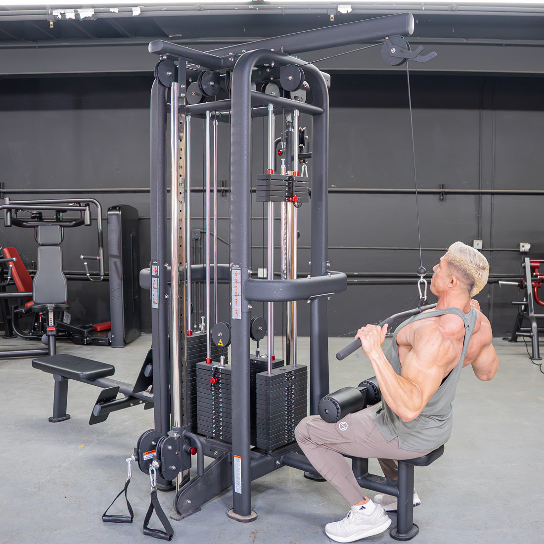 Man doing a low row exercise on a 4-stack jungle gym with multiple pulleys and weight stacks in a gym.