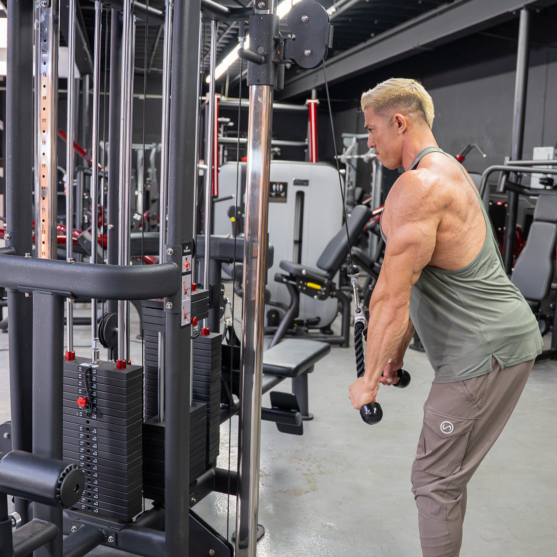 Muscular man doing tricep pushdowns on a black 4-stack cable jungle gym in a gym setting.