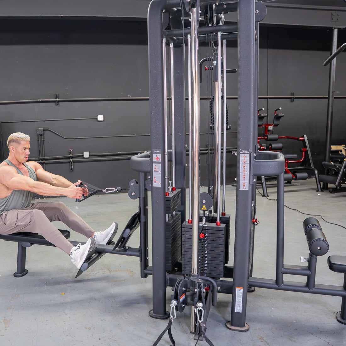 Man doing a low row on a 4-stack jungle gym machine with multiple weight stacks and pulleys in a gym.