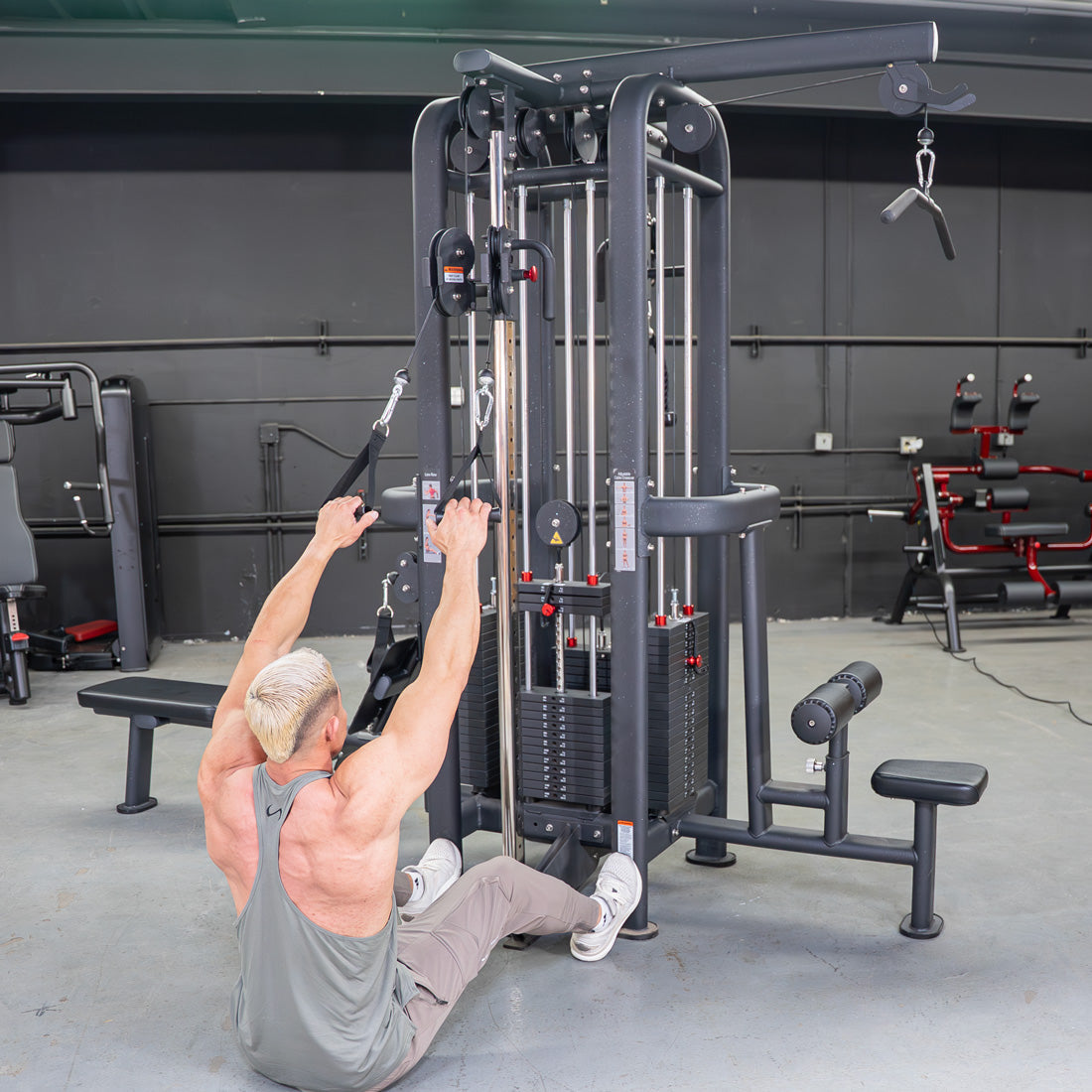 Man performing a low row exercise on a black 4-stack jungle gym with multiple pulleys and weight stacks.