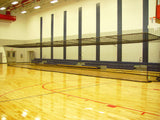 Black netting forming a large rectangular cage over a wooden gym floor with bleachers in the background.
