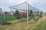Outdoor aluminum batting cage with black netting on a grassy field, houses and scoreboard in background.