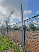 Outdoor batting cage net and chain-link fence next to a dirt field under a cloudy sky.