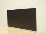 Black polyurethane foam wall pad installed on a light-colored wall above a wooden floor.