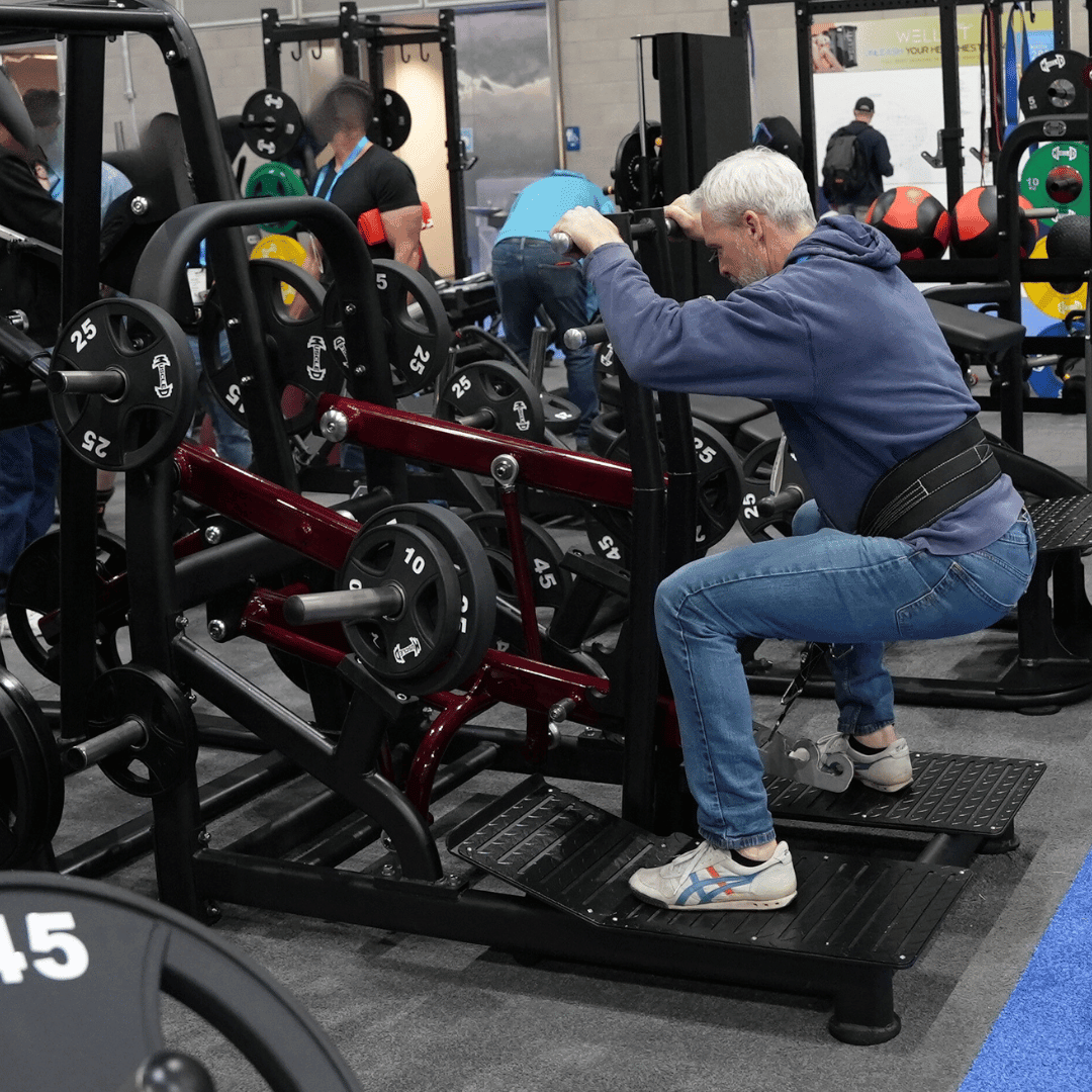 Man performing a belt squat on a plate-loaded machine in a gym.