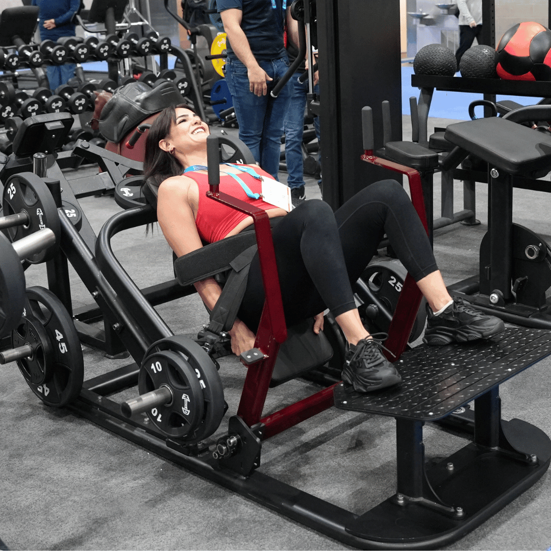 Woman in red top using a plate-loaded hip thruster machine in a gym, smiling.