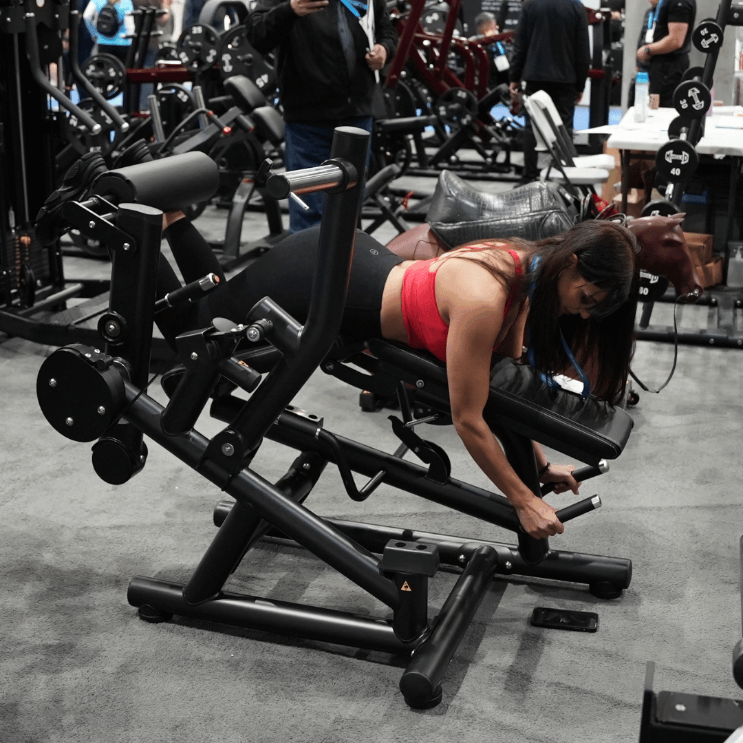 Woman performing leg curls on a black plate-loaded quad and hamstring machine.