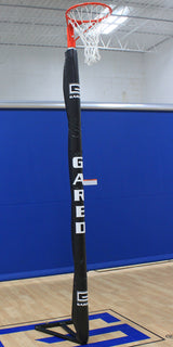 Portable netball system with an orange hoop, white net, and black padded pole on a gym court.