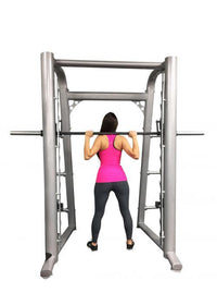 Thumbnail for Woman in pink top and black leggings using a silver Smith machine with a barbell on her shoulders.