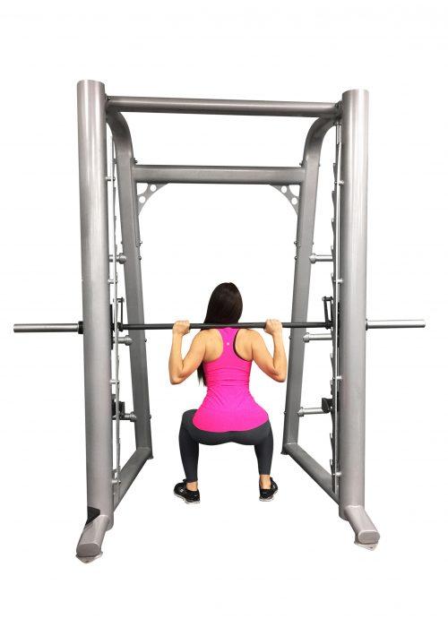Woman in pink top and black leggings squatting with a barbell on a silver Smith machine.