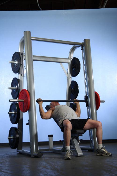 Man bench pressing on a Smith machine with plate storage.