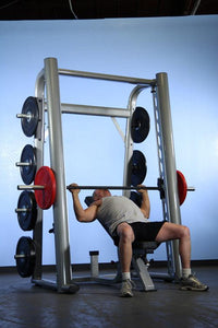 Thumbnail for Man bench pressing on a Smith machine with plate storage.