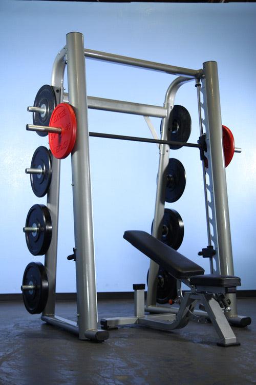 Silver Smith machine with black and red weight plates, a black barbell, and an adjustable black bench.