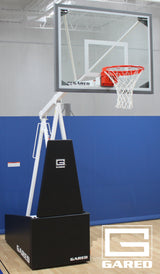 Portable basketball hoop with clear backboard, orange rim, and black base in a gym.