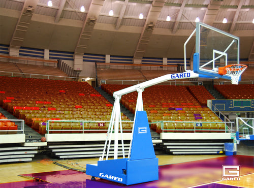 Portable basketball hoop with clear backboard and orange rim on a court in an empty arena.