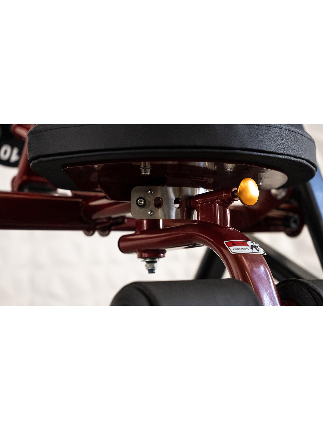 Close-up of a red fitness machine's black seat, yellow adjustment knob, and padded leg rests.