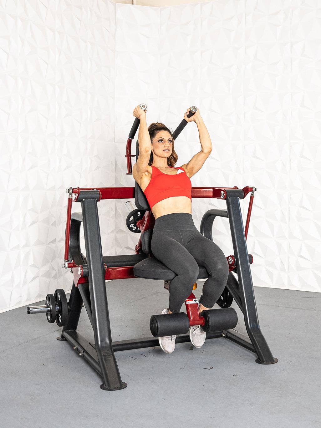 Woman in red top and gray leggings using a seated plate-loaded abdominal crunch machine.